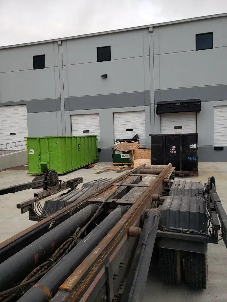 A commercial loading dock with dumpsters. A truck bed is in the foreground. Building exterior has garage doors.