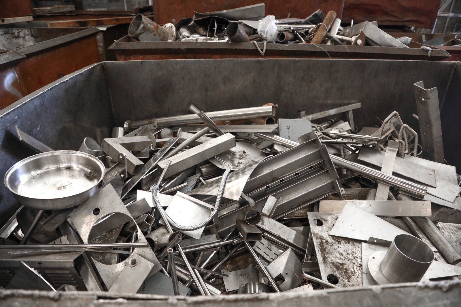 Bin of scrap metal, including a mixing bowl, rods, and flat pieces, in an industrial setting.
