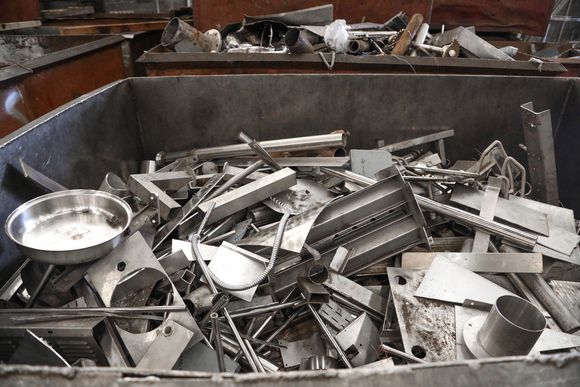 Bin of scrap metal, including a mixing bowl, rods, and flat pieces, in an industrial setting.