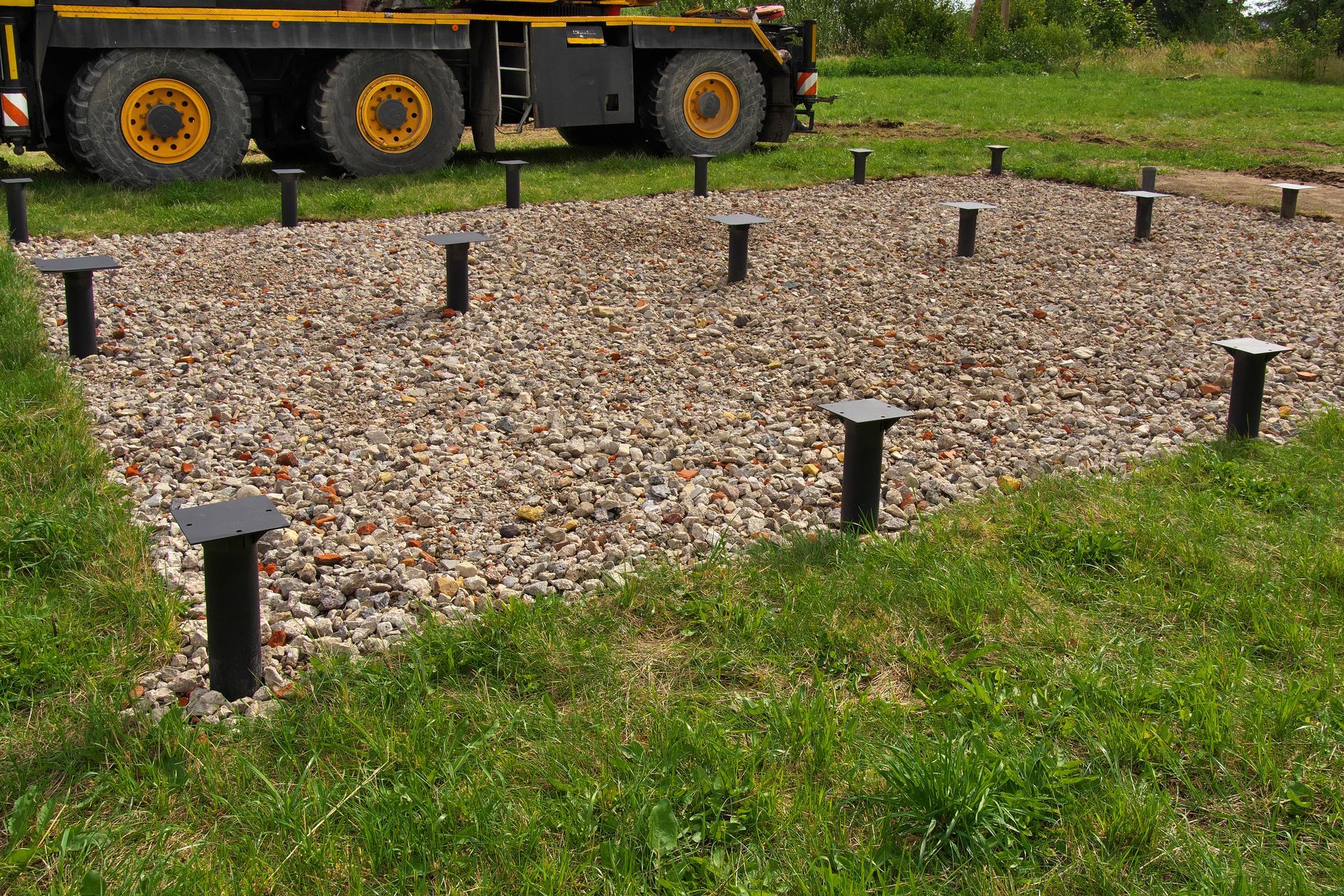 Fondations en gravier avec des poteaux noirs dans une cour herbeuse à côté d'une remorque de camion.