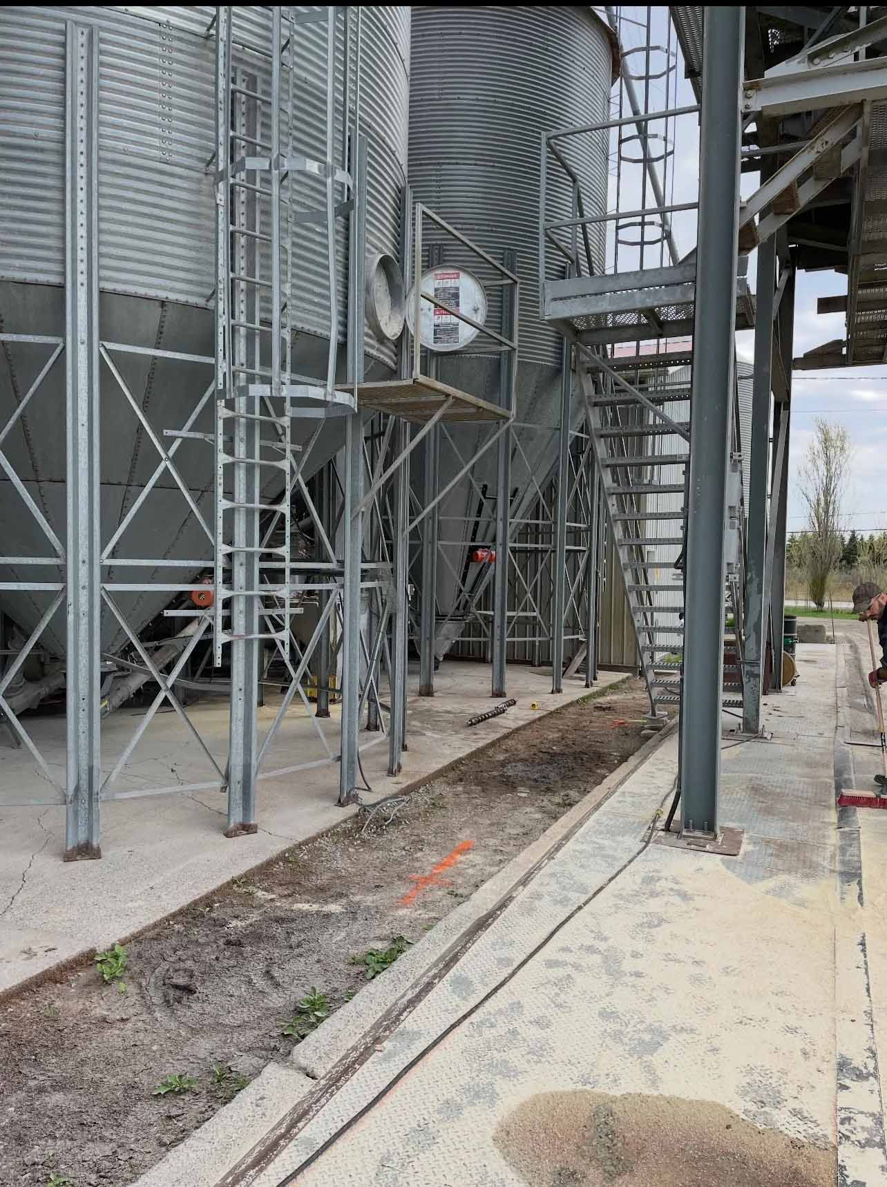 Silos industriels et charpentes métalliques bordant une voie ferrée étroite en gravier sur un chantier de construction