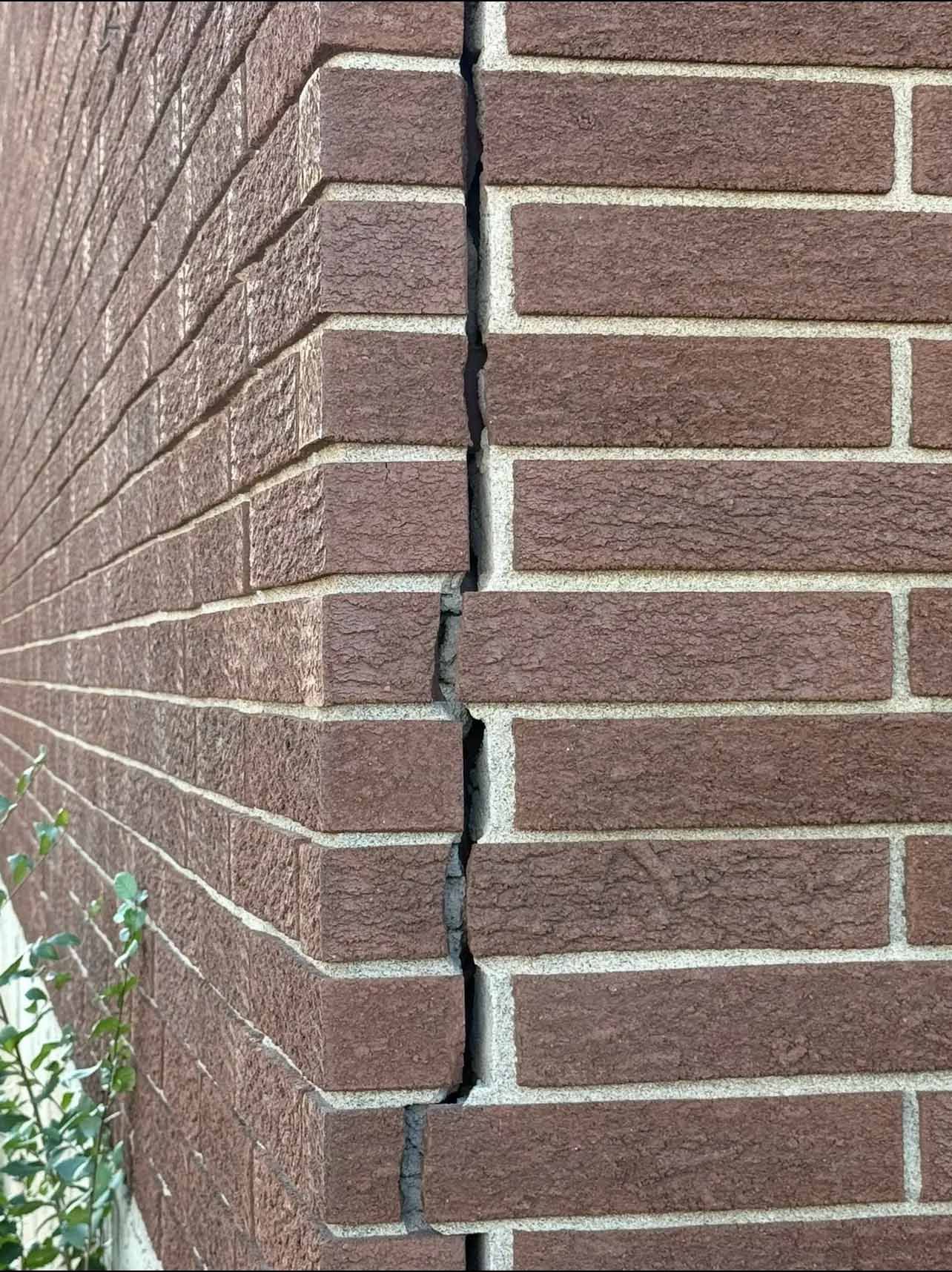 Coin de mur en briques fissuré avec une fente verticale dans le mortier