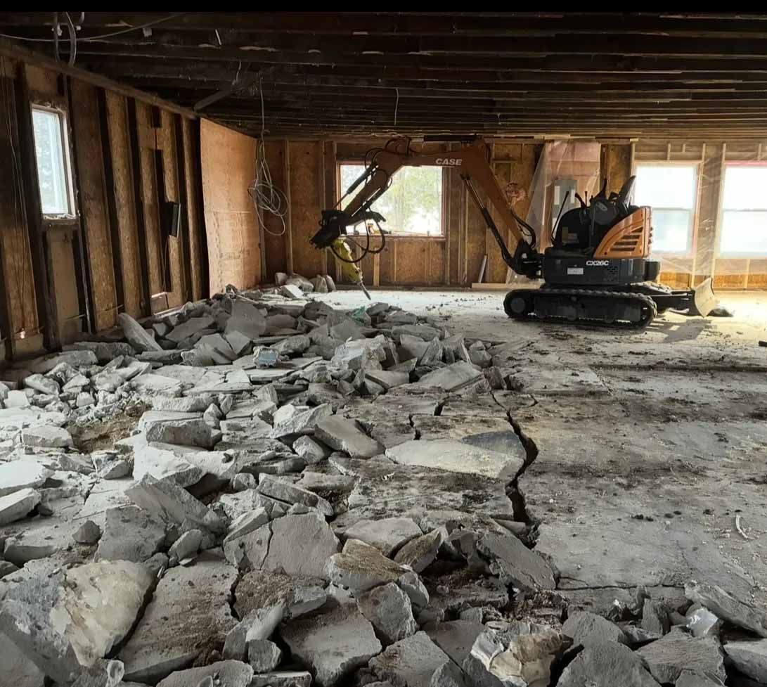 Une équipe de construction démolit un sol en béton à l'intérieur d'un bâtiment endommagé et inachevé, dont les décombres sont éparpillés dans la pièce.
