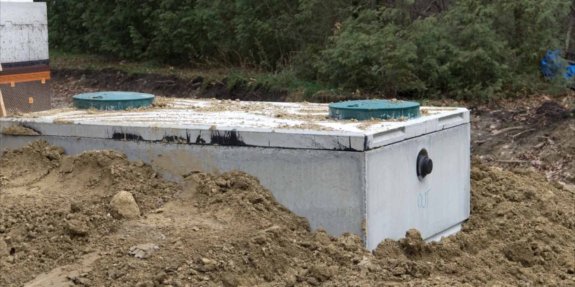 Fosse septique en béton avec couvercles bleus, partiellement enterrée sur un chantier de construction