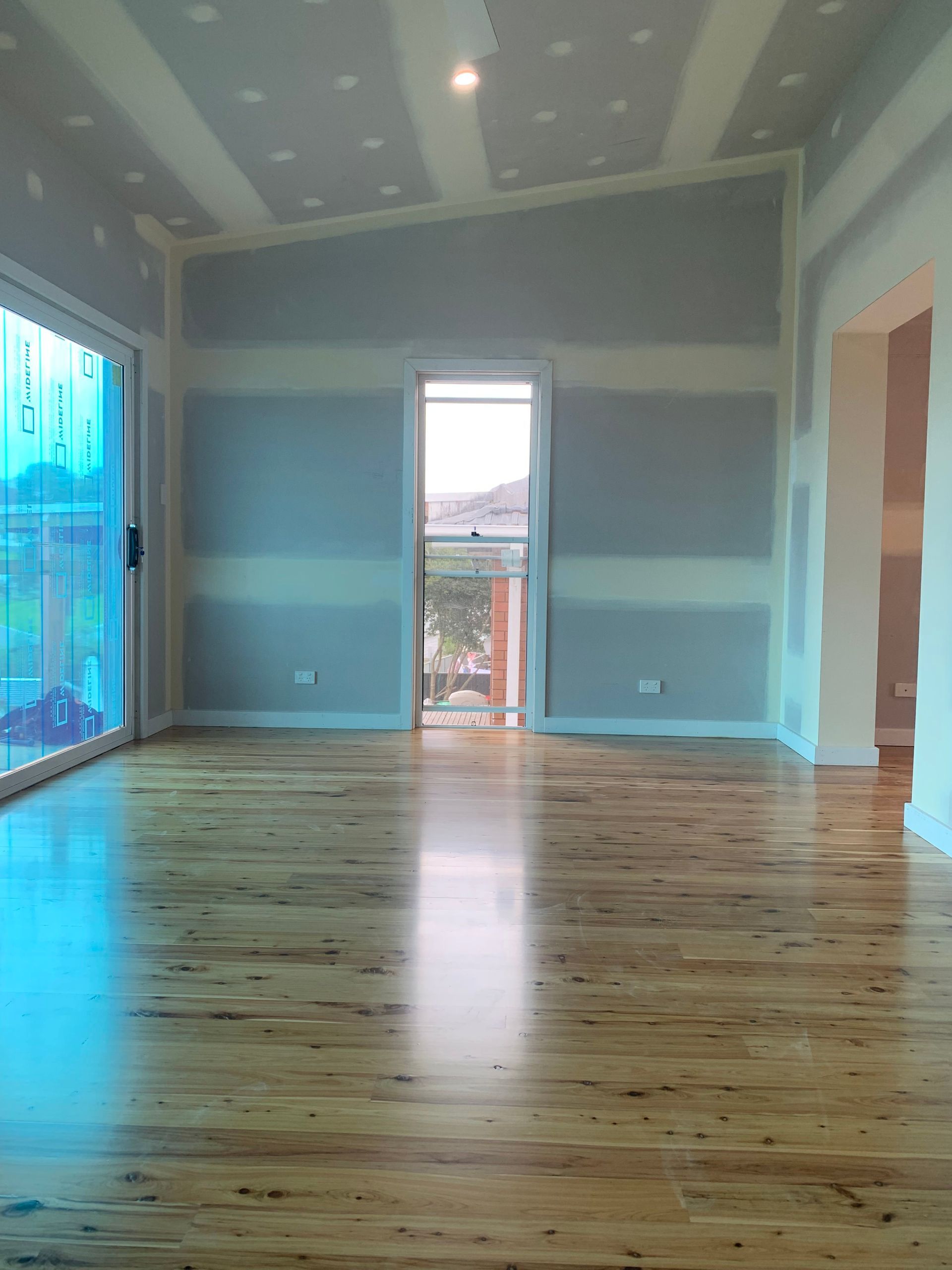 Interior under renovation, with exposed drywall, stacked lumber, and open sliding door to a yard.