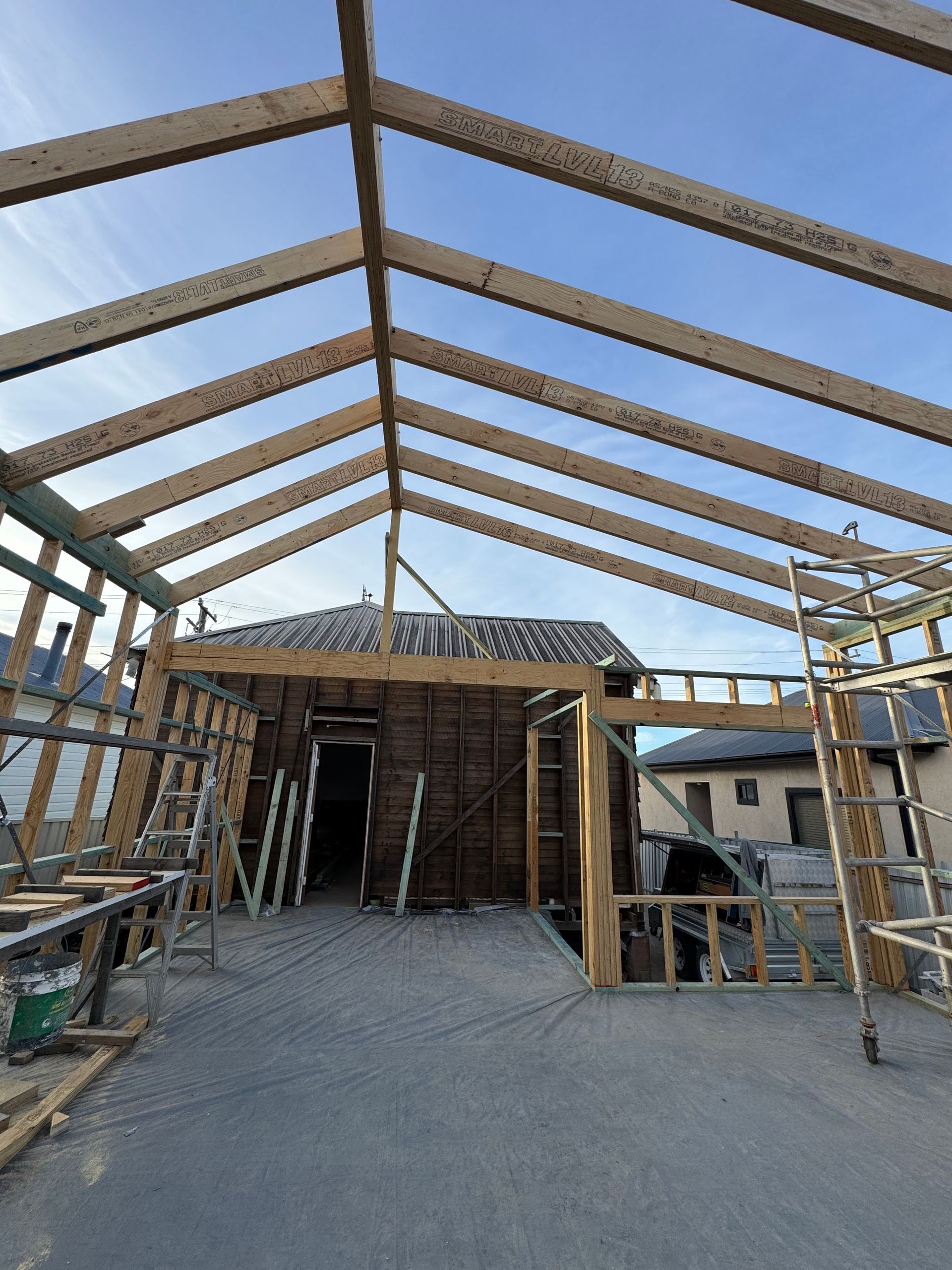 Construction of a wooden roof structure over a building. The framework is incomplete, and the sky is visible through the open roof.