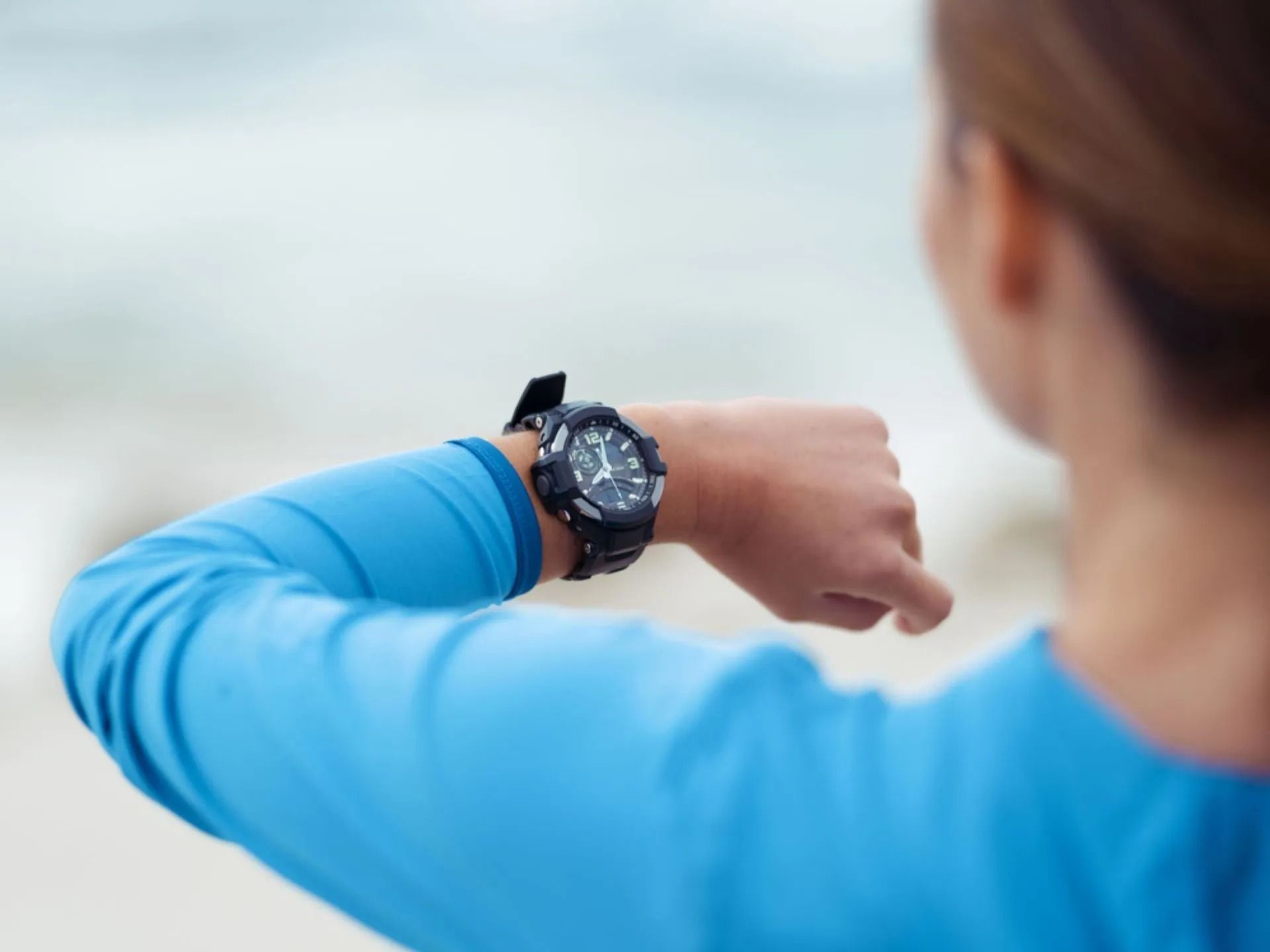 Woman in Blue Athletic Shirt Checks Watch Outdoors Near Blurred Beach — Coastal Clocks & Watches in Mooloolaba, QLD