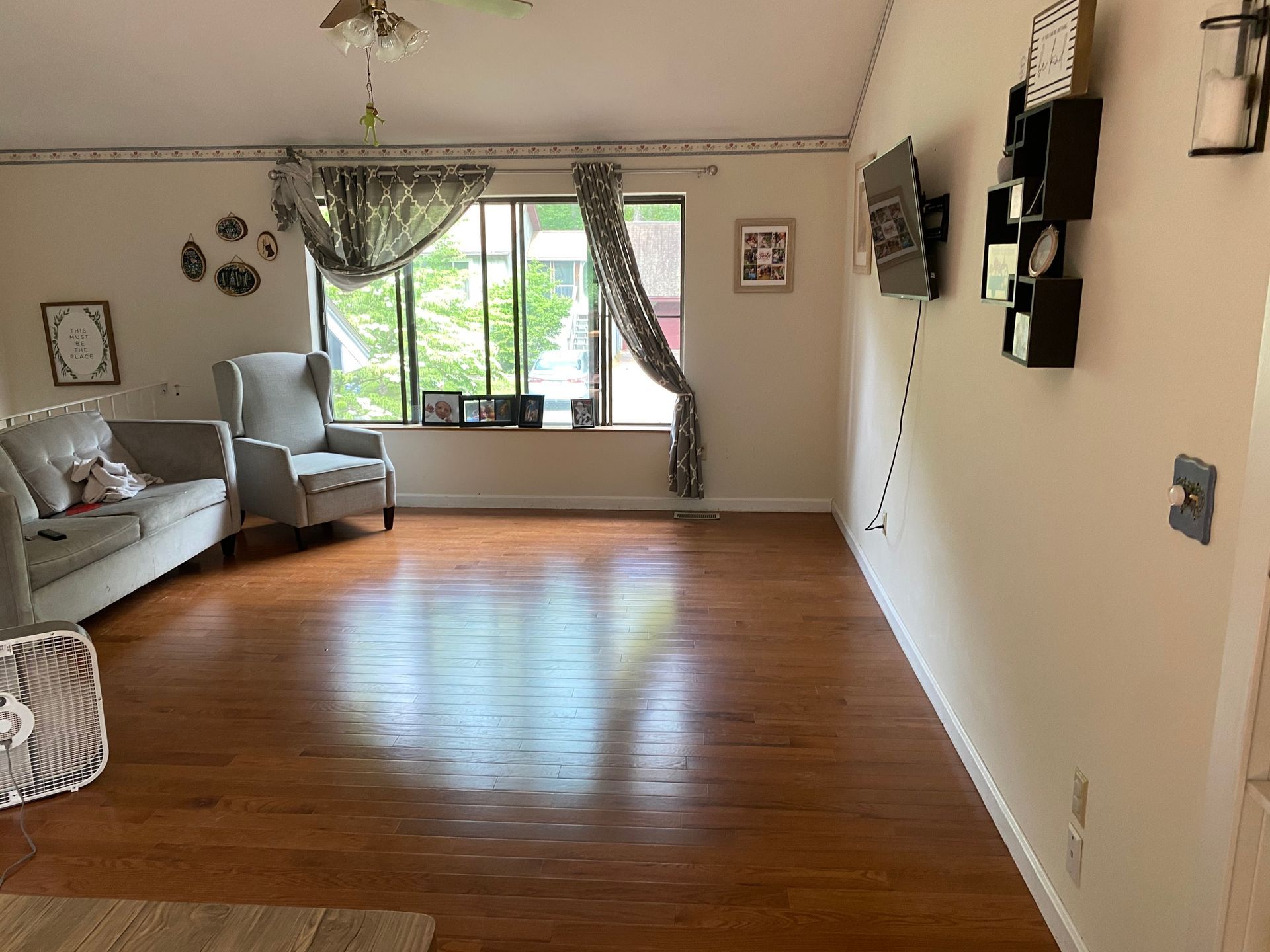 A living room with hardwood floors , a couch , chair and television.