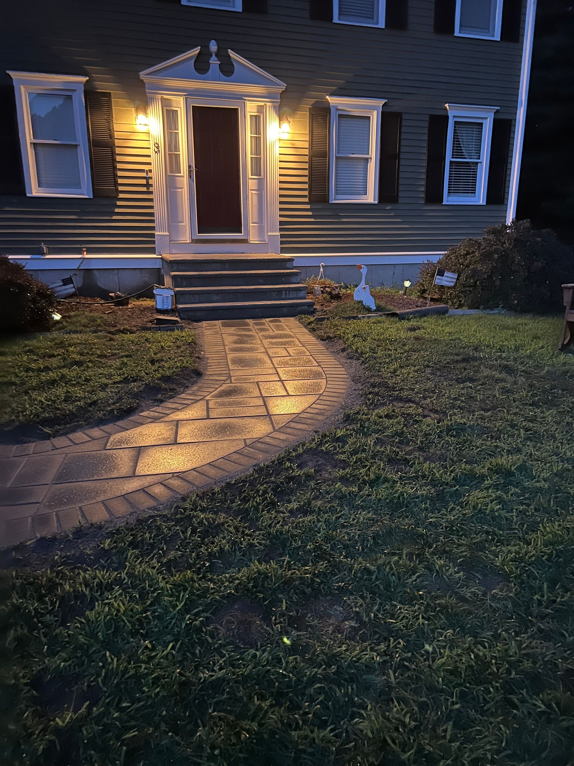 A house with a walkway leading to the front door is lit up at night.