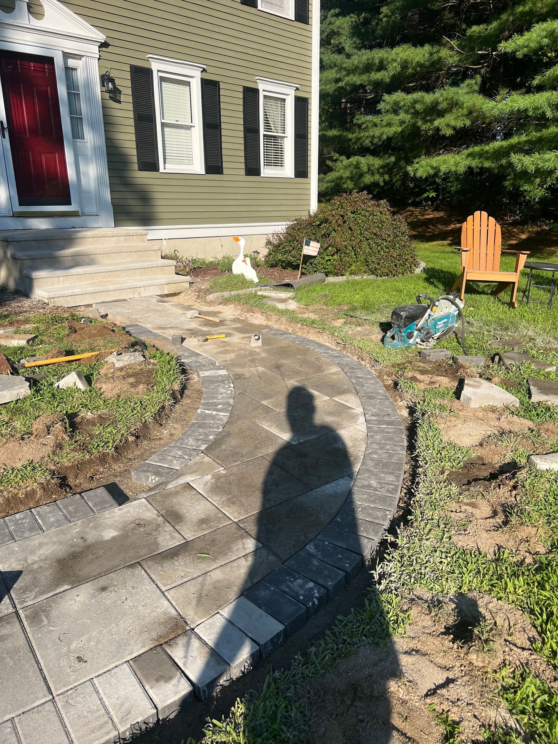 A shadow of a person is cast on a brick walkway in front of a house.