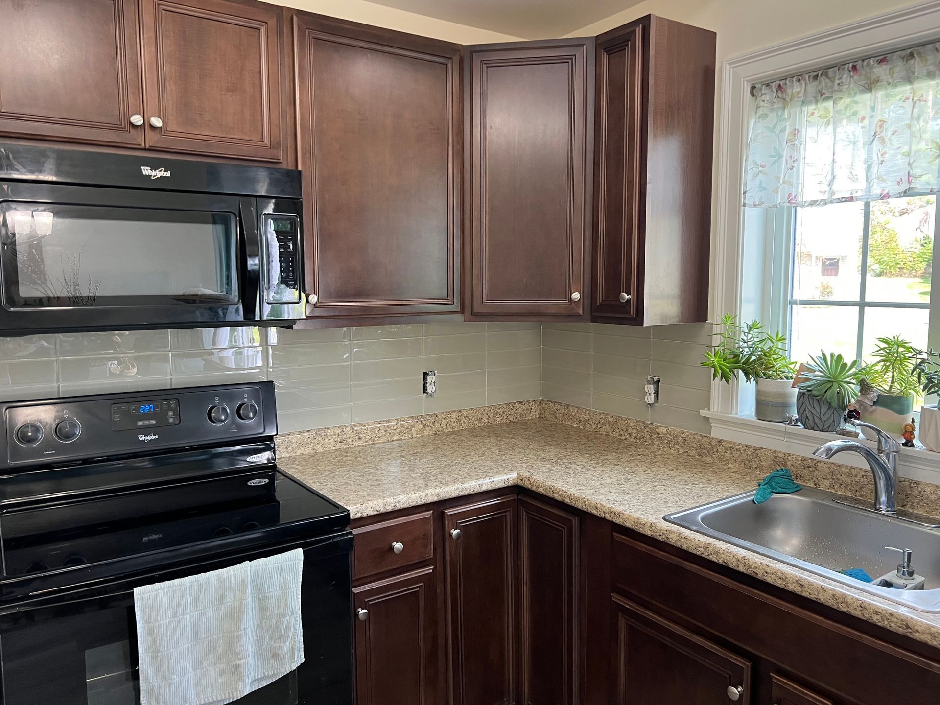 A kitchen with a stove , microwave , sink and window.
