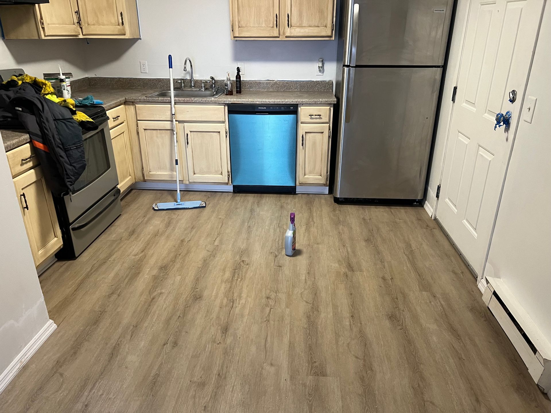 A kitchen with wooden floors , stainless steel appliances , and a mop on the floor.
