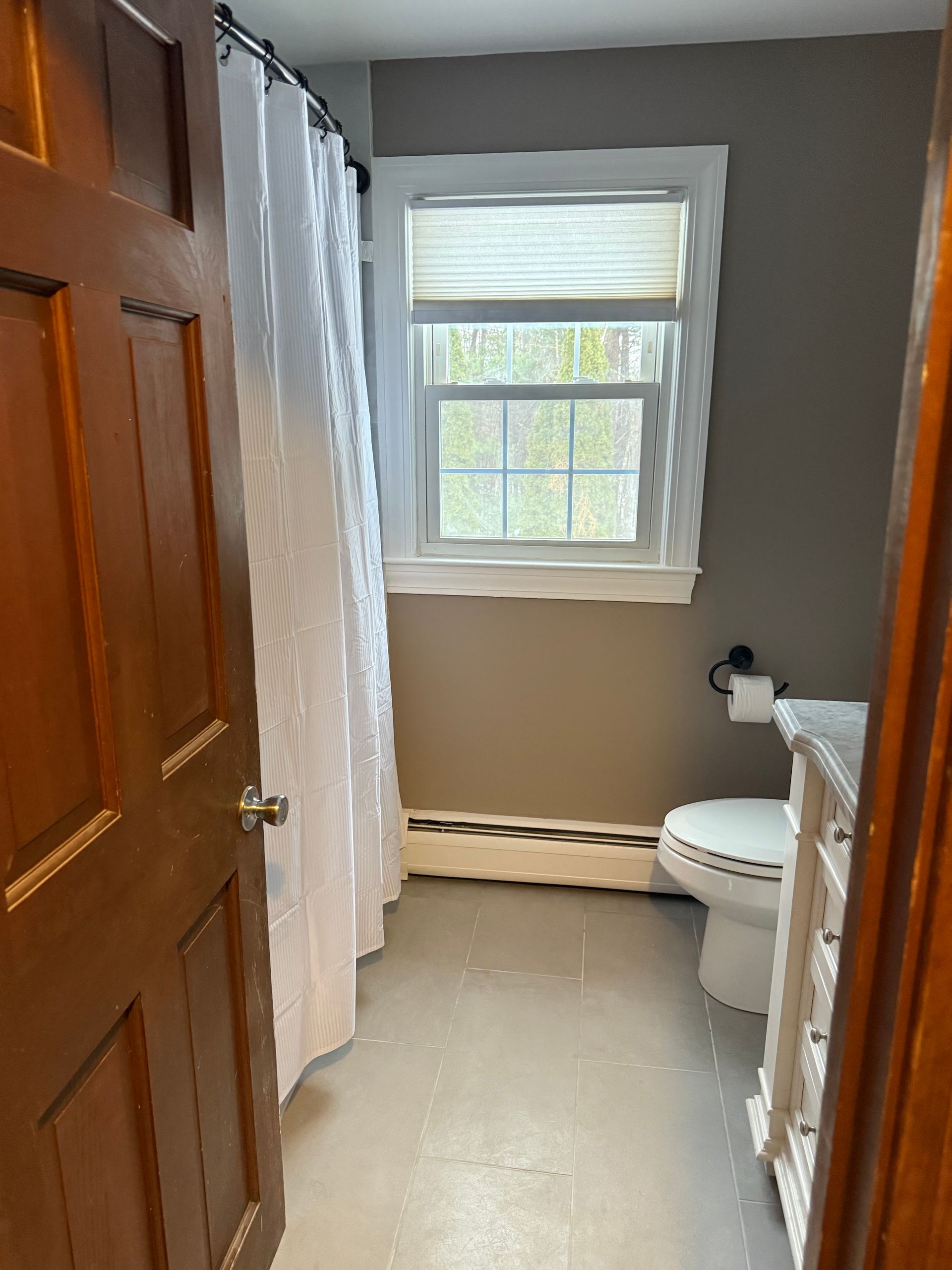 A bathroom with a toilet , sink , shower curtain and window.