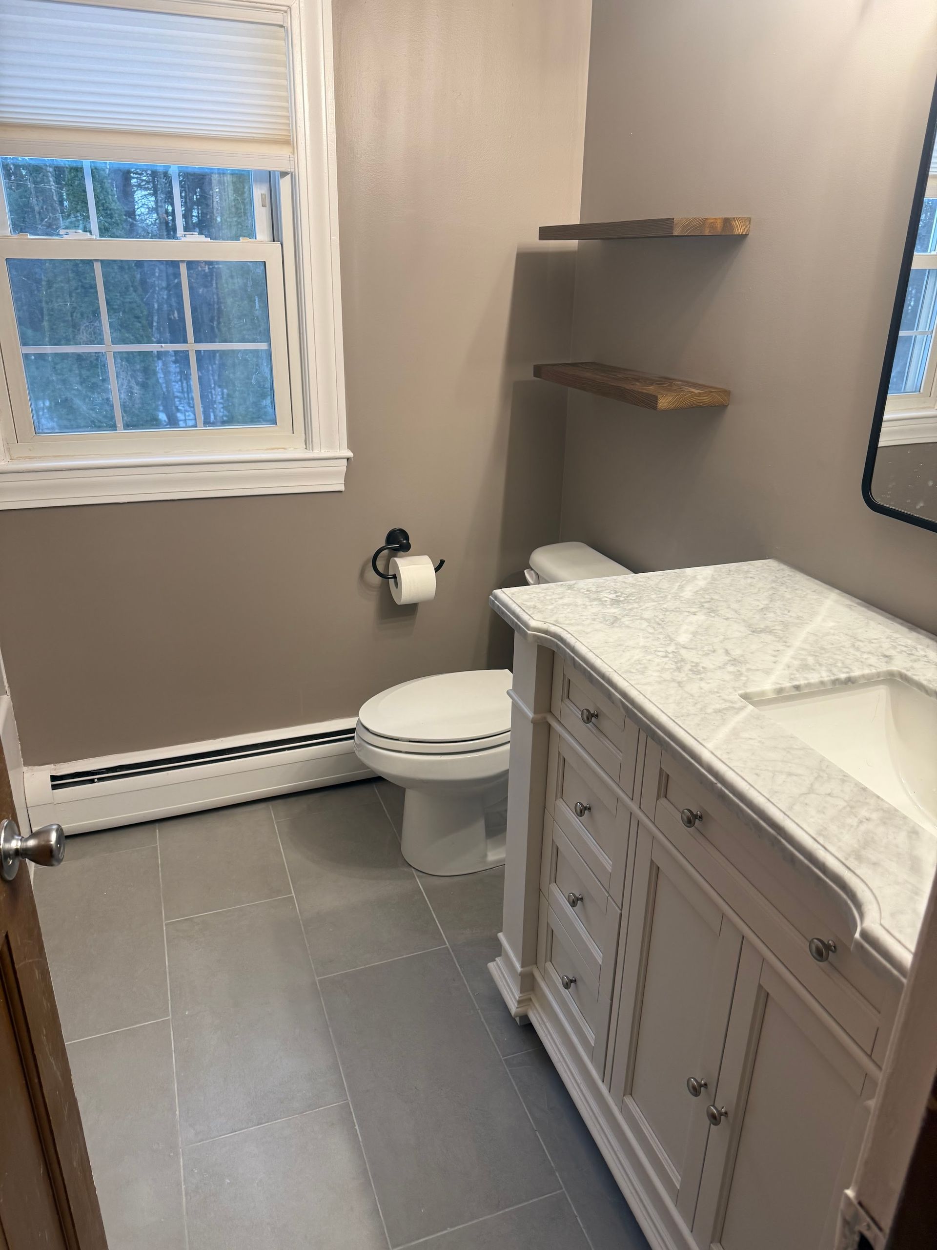A bathroom with a toilet , sink , mirror and window.