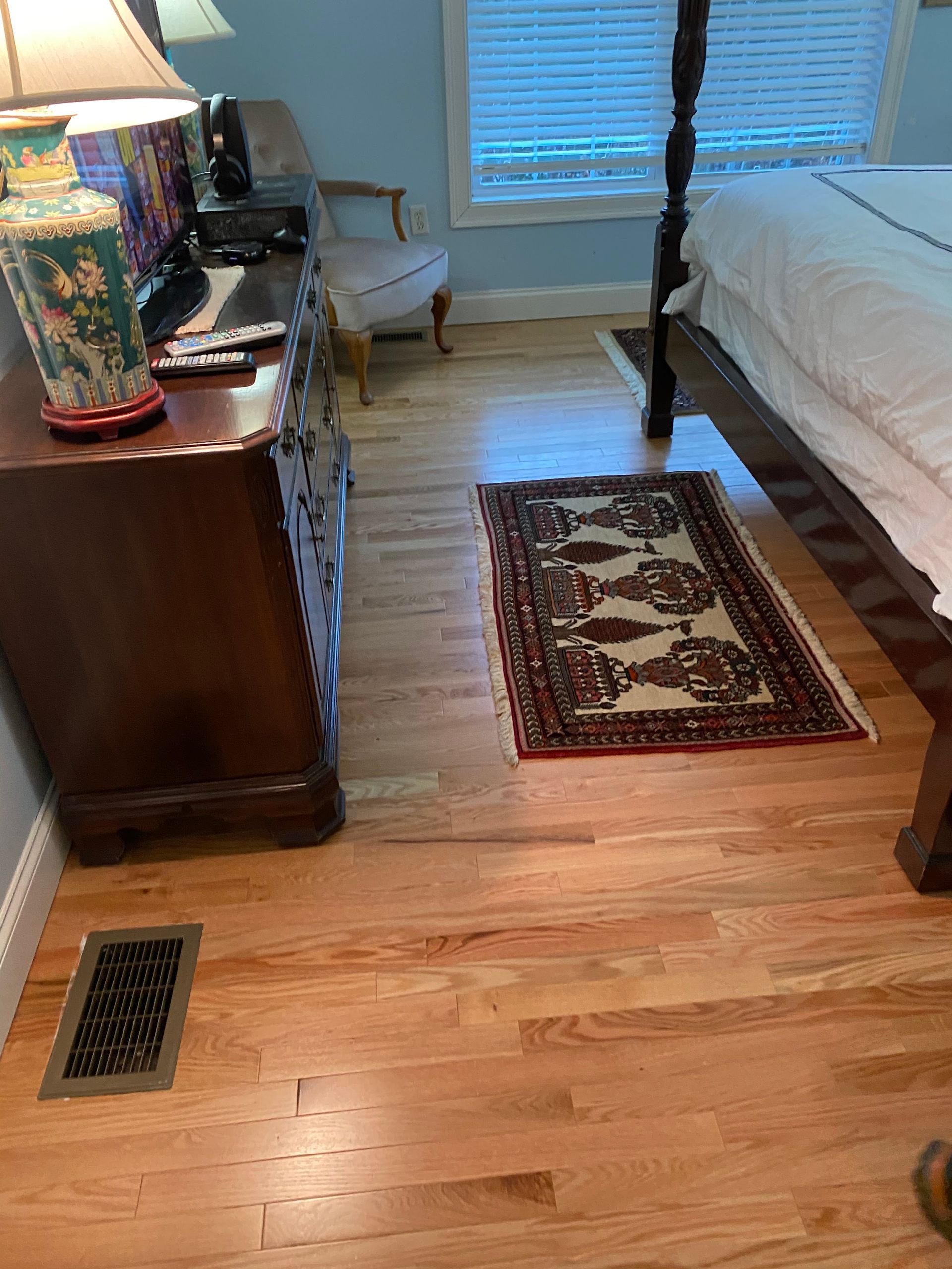 A bedroom with hardwood floors , a bed , dresser , lamp and rug.