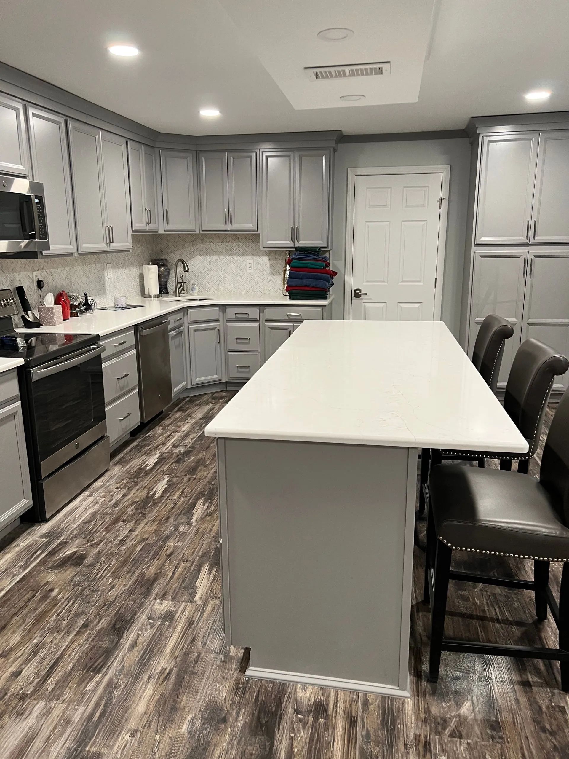 Modern kitchen featuring gray cabinets, white countertops, a central island with bar stools, and wood-patterned flooring.