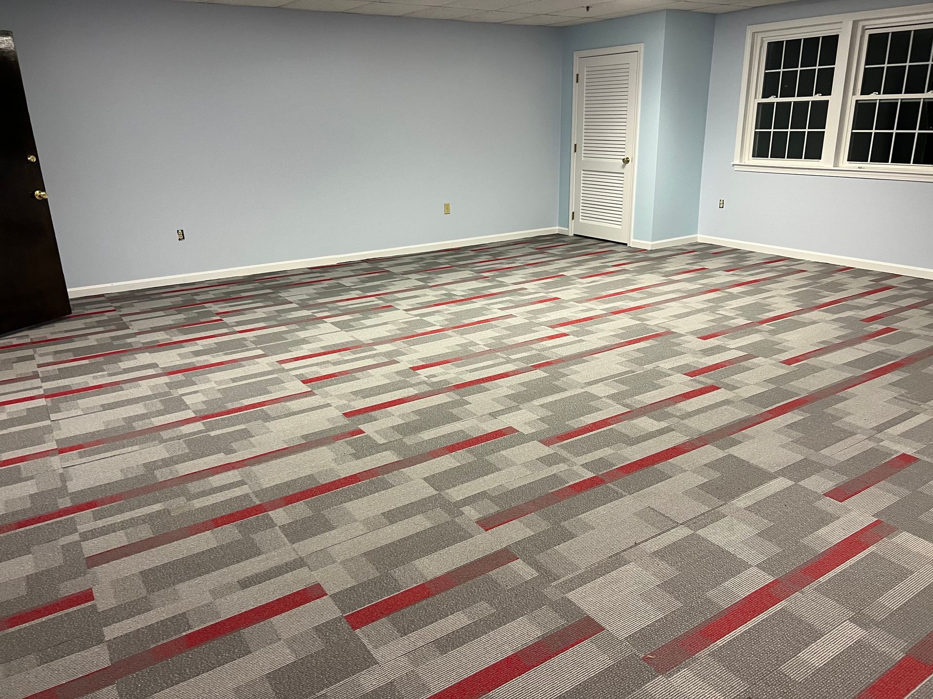 A large room with a carpeted floor and two windows.