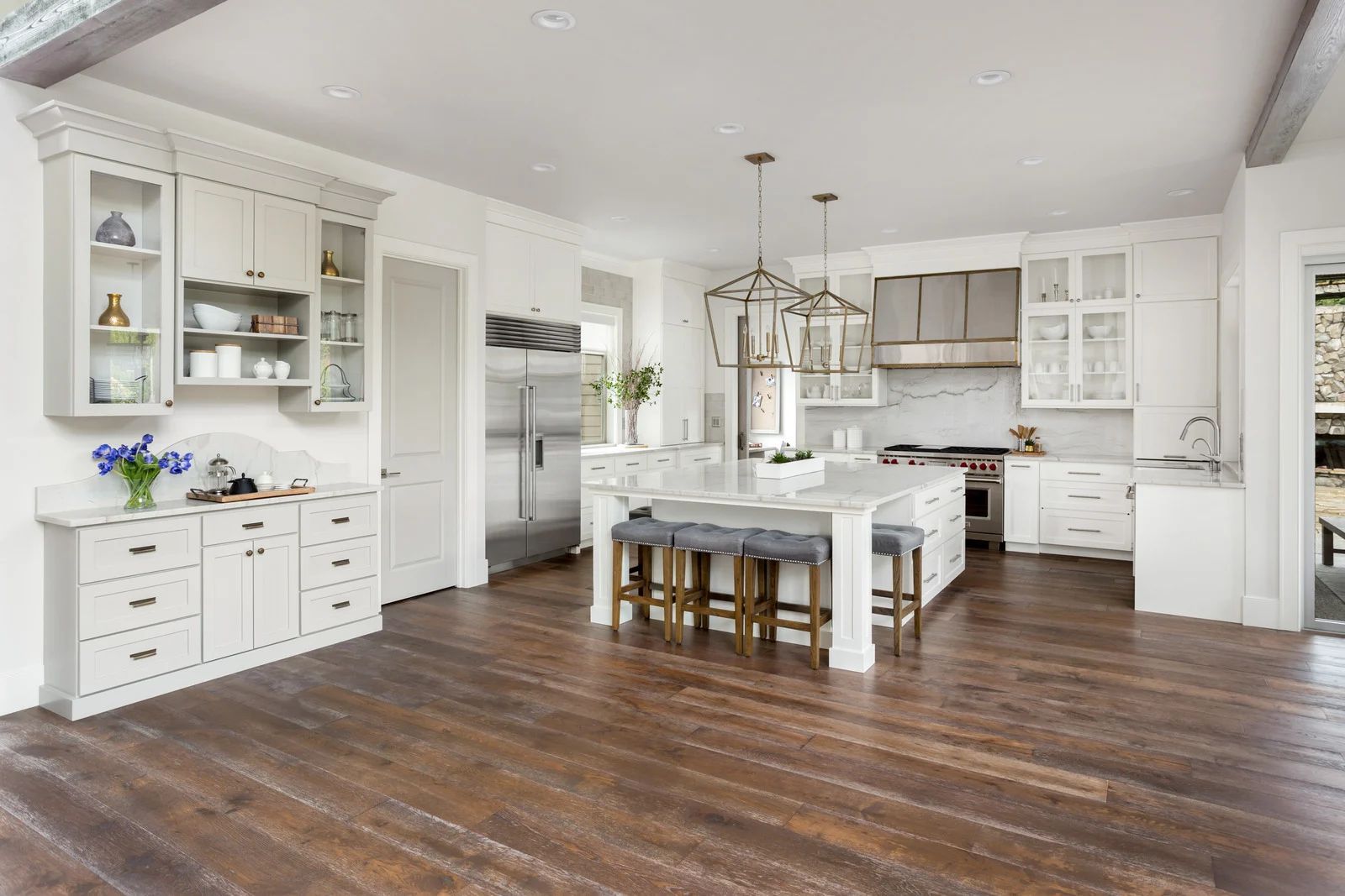 Spacious white kitchen with a large island, stainless steel appliances, and dark wood flooring.