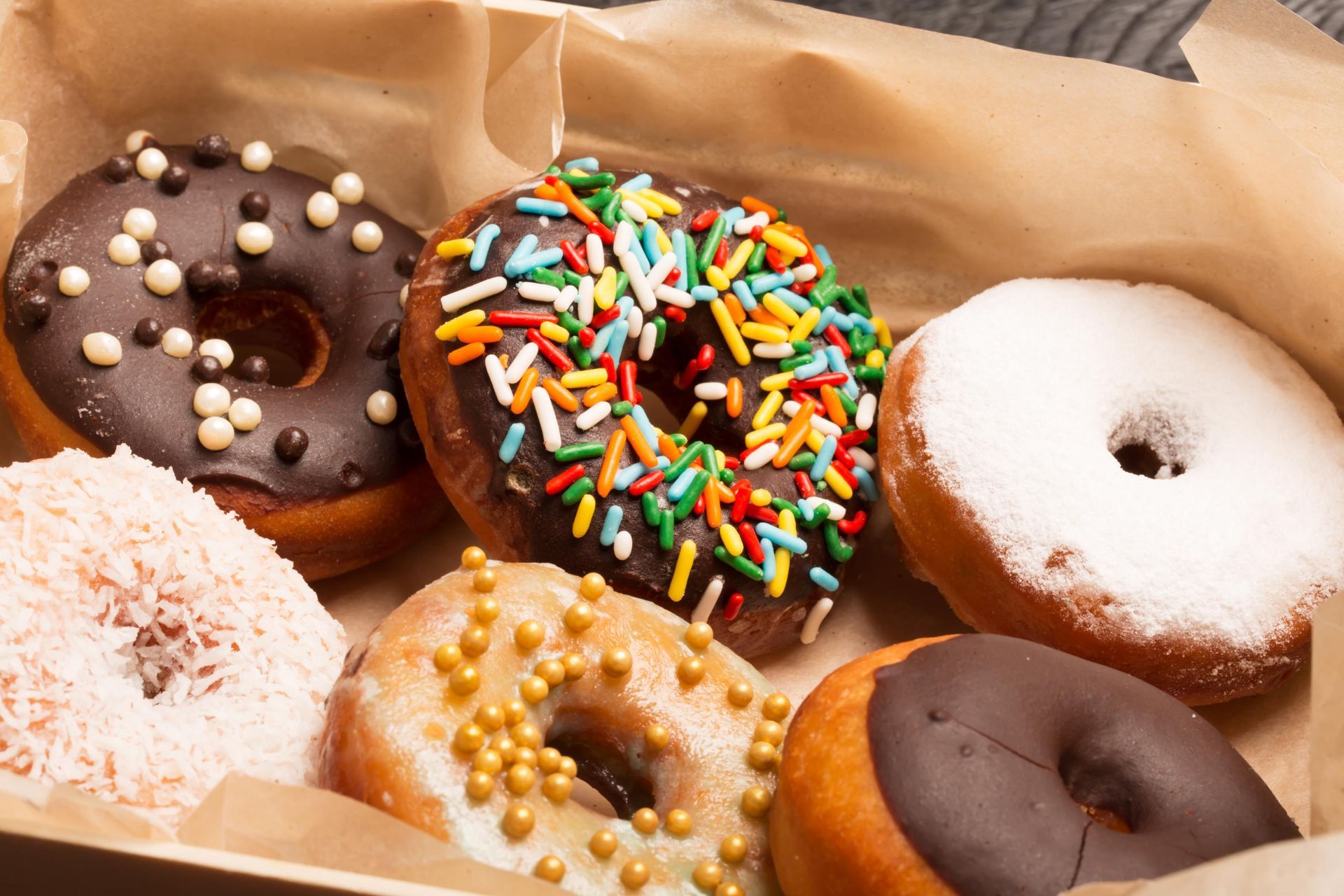 Box of assorted donuts: chocolate frosted, sprinkle-covered, powdered sugar, and coconut.