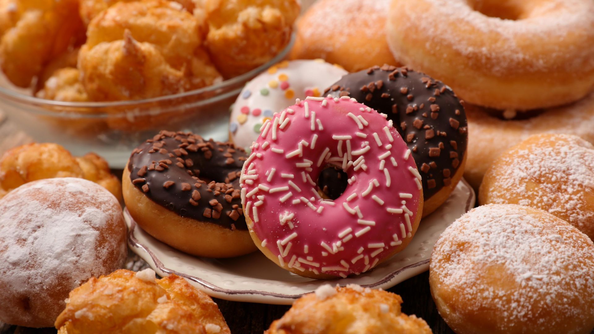 Assortment of doughnuts with various toppings, including chocolate and sprinkles. Some are powdered.