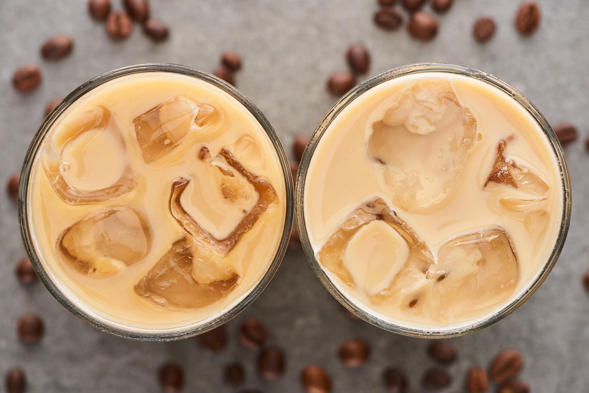Two iced coffee drinks with ice cubes, coffee beans scattered around.