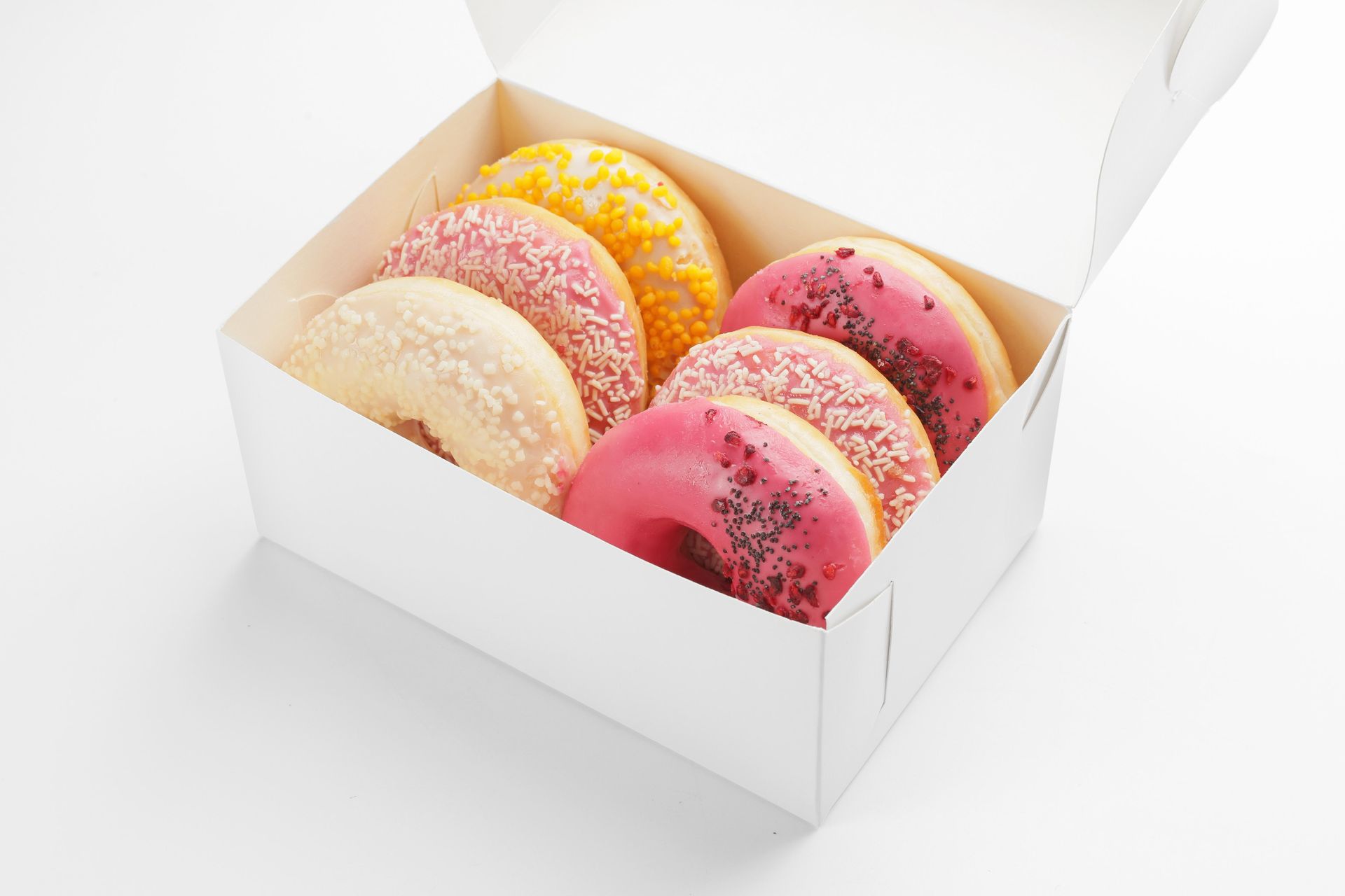 Box of assorted donuts: pink, yellow, and white frosting with sprinkles.