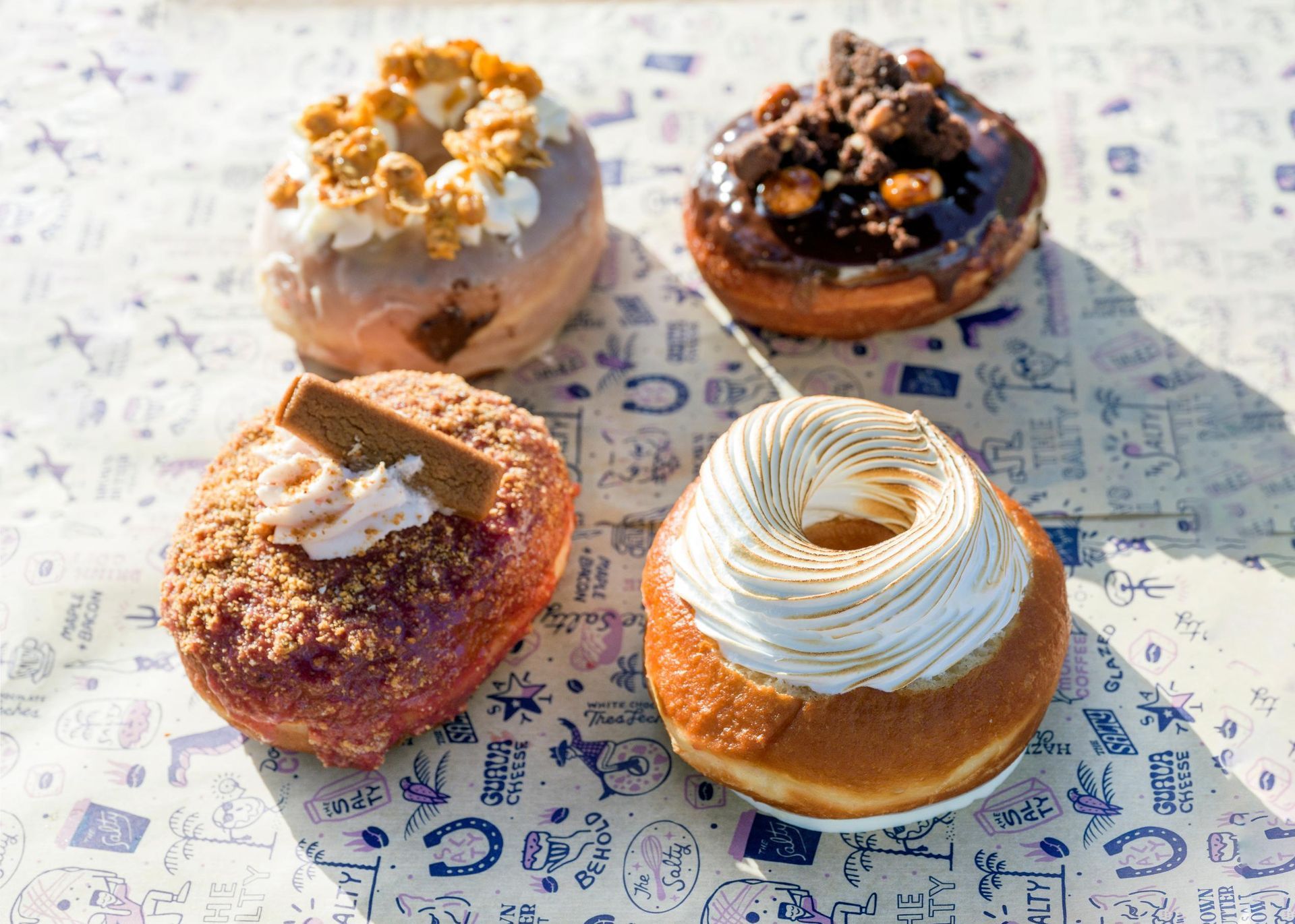 Four gourmet donuts: caramel popcorn, chocolate nut, cookie crumble, and meringue.