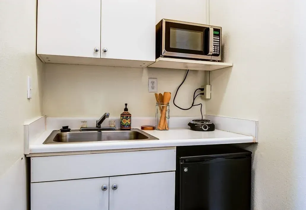 a small kitchen with a sink , microwave , and trash can .
