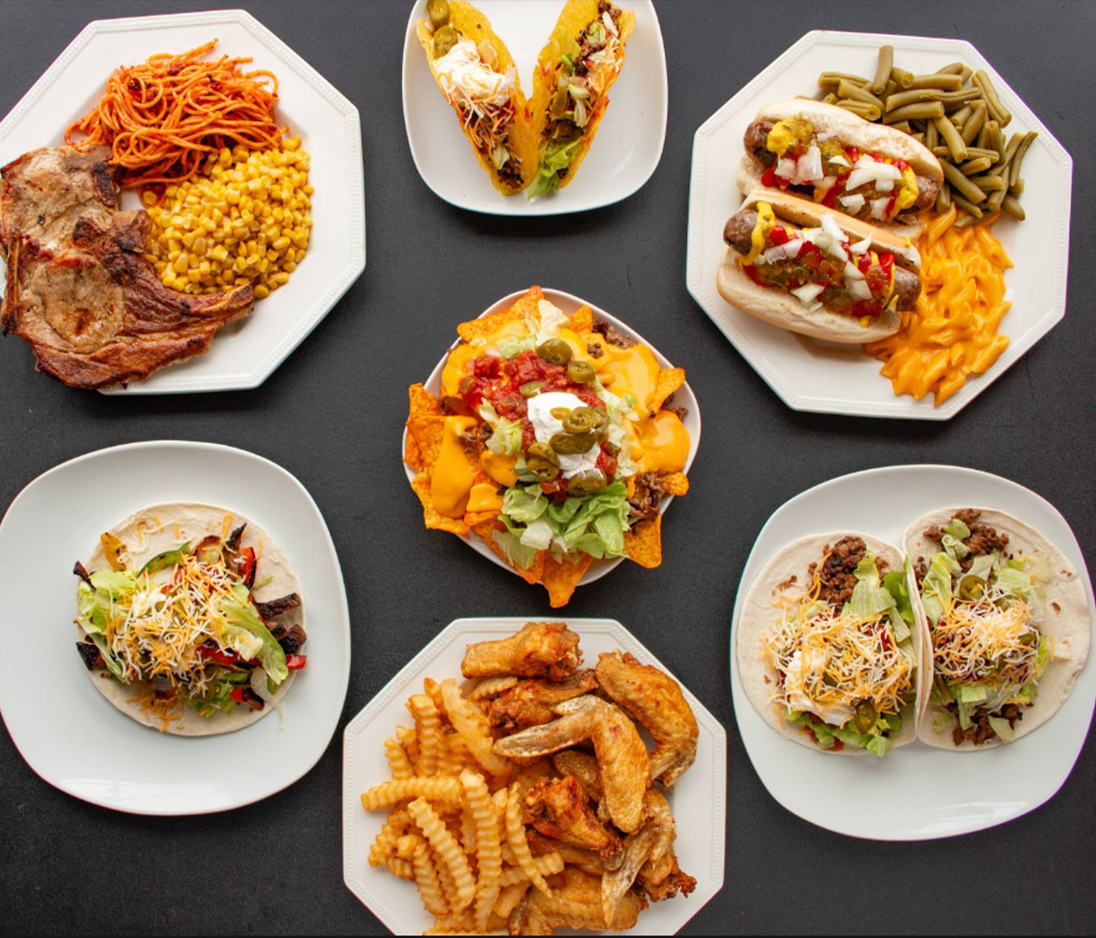 A table topped with plates of food including tacos and hot dogs