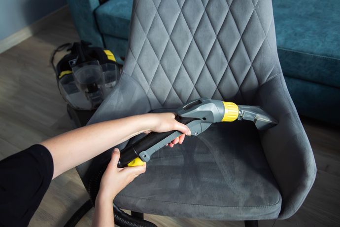 Close-up of hands using a washing vacuum to perform upholstery cleaning on a gray chair. Close-up of hands using a washing vacuum to perform upholstery cleaning on a gray chair.