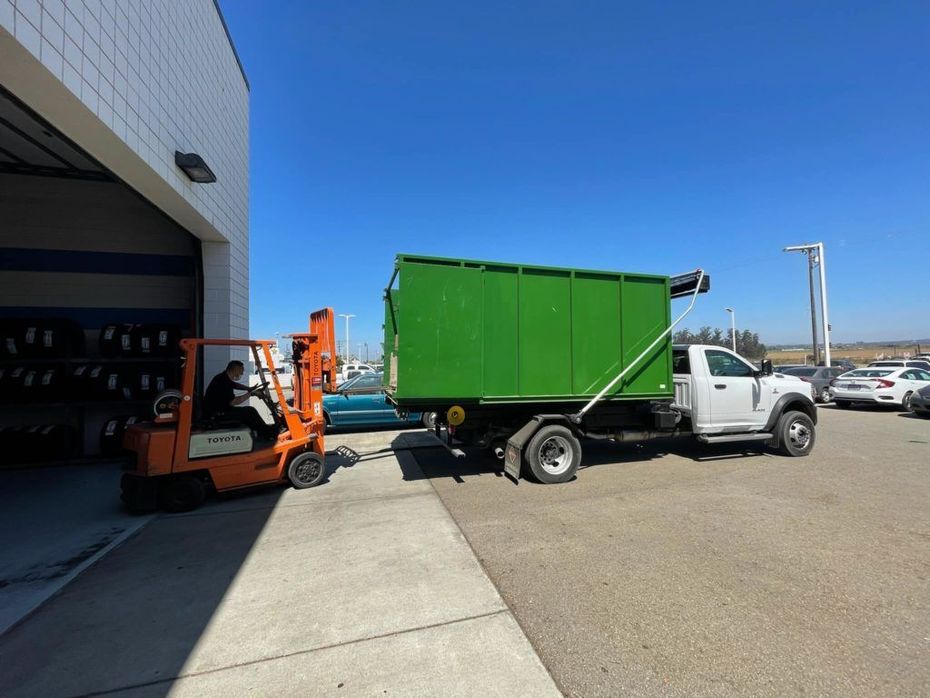 A dump truck is being towed by a forklift in a parking lot.