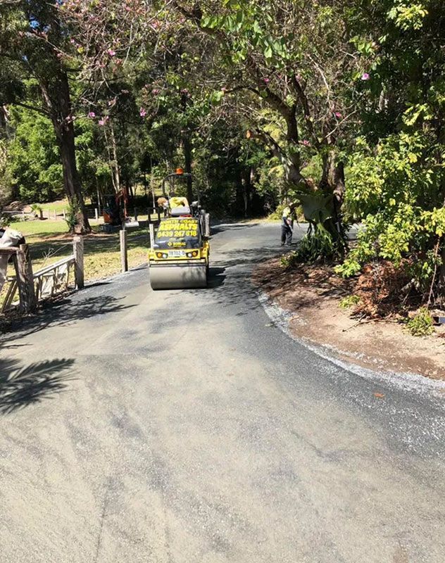 A Yellow Truck is Driving Down a Road Surrounded by Trees — North Coast Asphalts in Corindi Beach, NSW