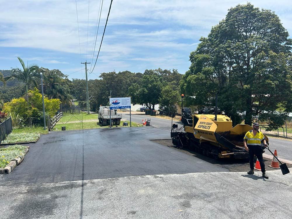 A Man is Standing Next to a Yellow Asphalt Paving Machine — North Coast Asphalts in Corindi Beach, NSW