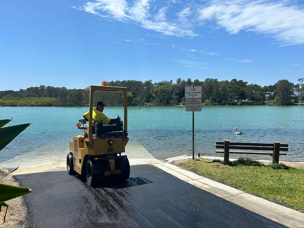 A Man is Driving a Forklift on a Road Near a Lake — North Coast Asphalts in Corindi Beach, NSW