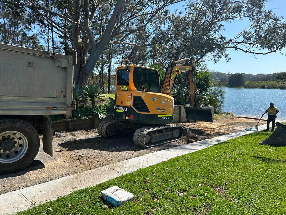 A Yellow Excavator is Parked on the Side of the Road Next to a Dump Truck — North Coast Asphalts in Corindi Beach, NSW