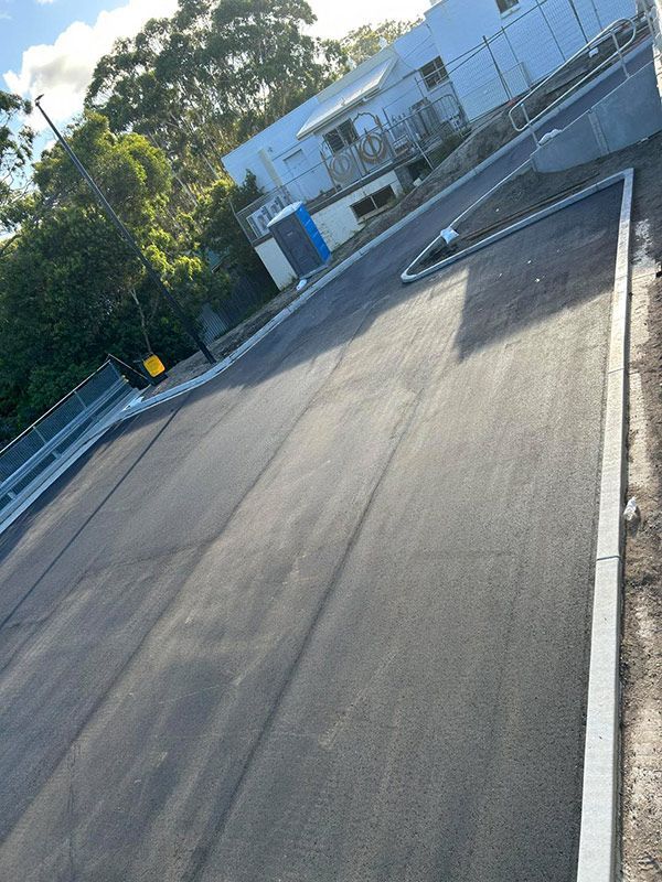 A Black Asphalt Road With a White Building in the Background — North Coast Asphalts in Clarence Valley, NSW