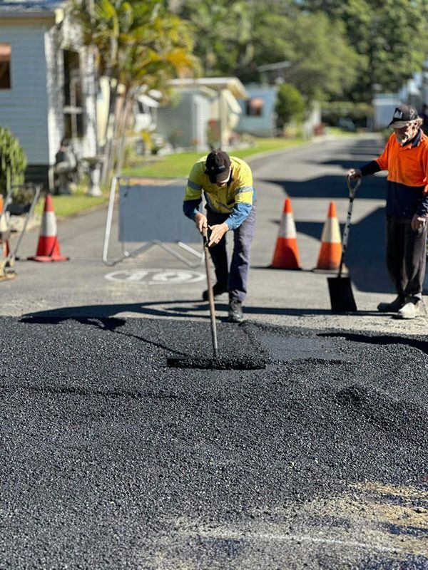 A Man is Using a Broom to Spread Asphalt on a Road — North Coast Asphalts in Corindi Beach, NSW