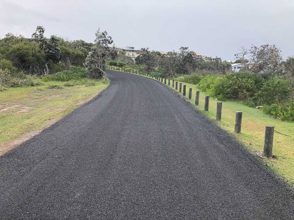 A Black Road With a Wooden Fence Along the Side of It — North Coast Asphalts in Corindi Beach, NSW