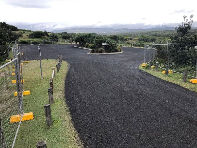 A Black Road With a Yellow Fence on the Side of It — North Coast Asphalts in Corindi Beach, NSW