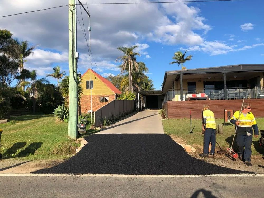 A Couple of Men Are Standing on the Side of a Road Next to a House — North Coast Asphalts in Corindi Beach, NSW