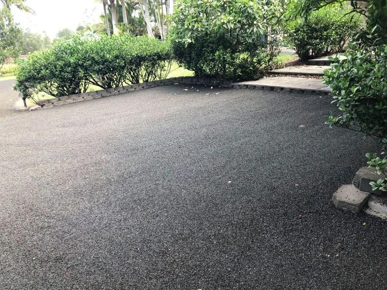 A Black Asphalt Driveway Surrounded by Trees and Bushes — North Coast Asphalts in Corindi Beach, NSW