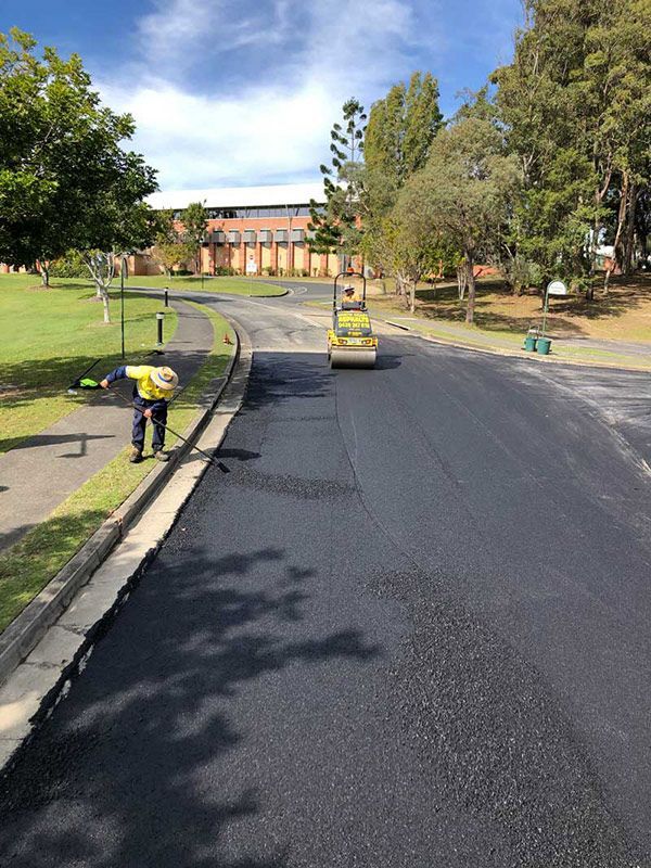 A Man is Laying Asphalt on the Side of a Road — North Coast Asphalts in Corindi Beach, NSW
