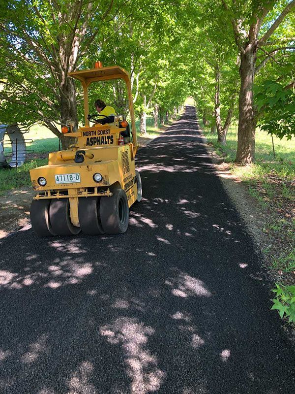 A Yellow Asphalt Roller is Driving Down a Road — North Coast Asphalts in Corindi Beach, NSW