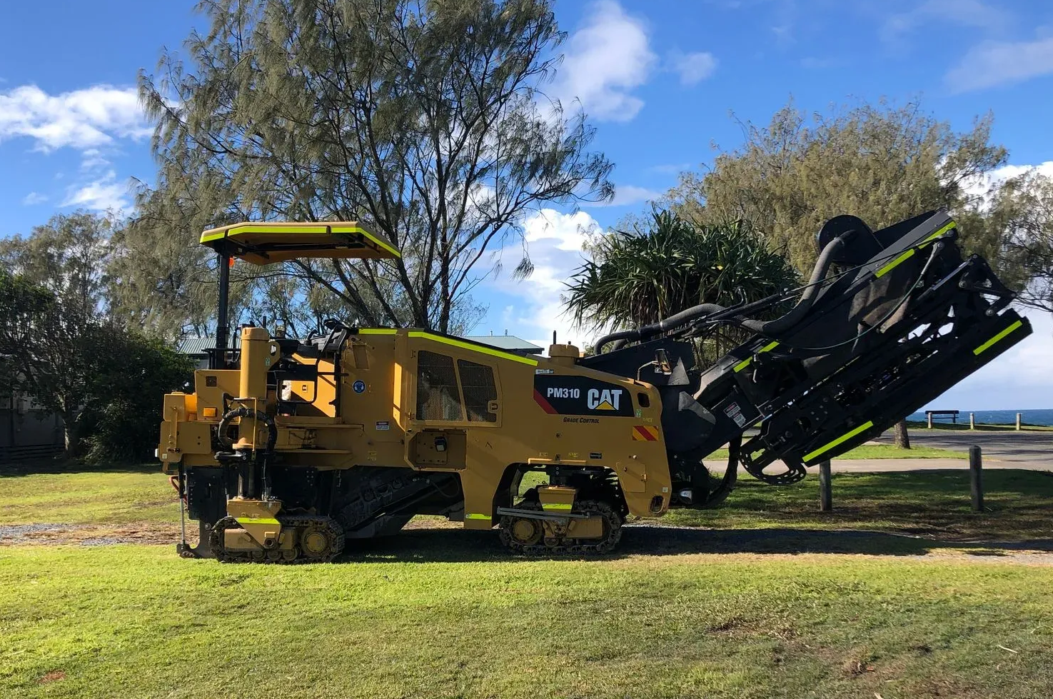 Yellow Caterpillar road milling machine on grass near the beach.— North Coast Asphalts in Corindi Beach, NSW