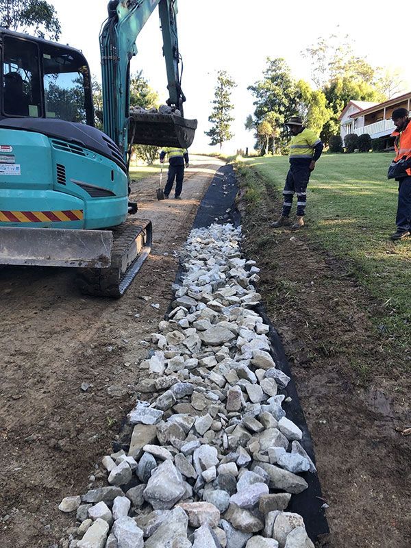 A Man is Standing Next to a Large Pile of Rocks Next to an Excavator — North Coast Asphalts in Corindi Beach, NSW
