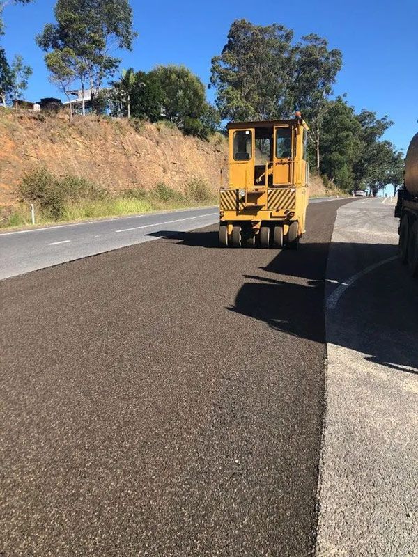 A Yellow Truck is Driving Down a Road With Trees in the Background — North Coast Asphalts in Corindi Beach, NSW