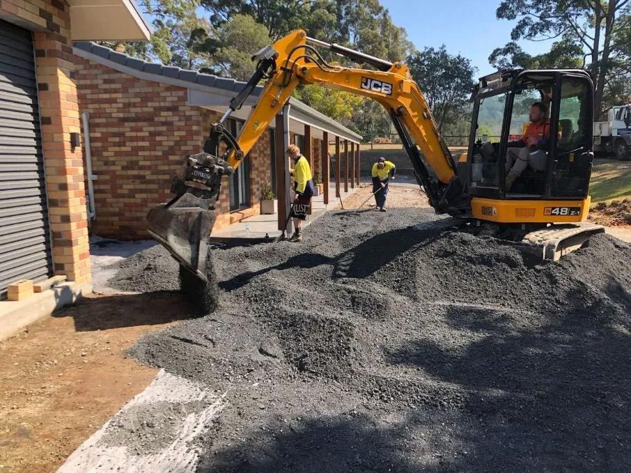 A Yellow Excavator is Digging a Hole in the Ground in Front of a House — North Coast Asphalts in Corindi Beach, NSW