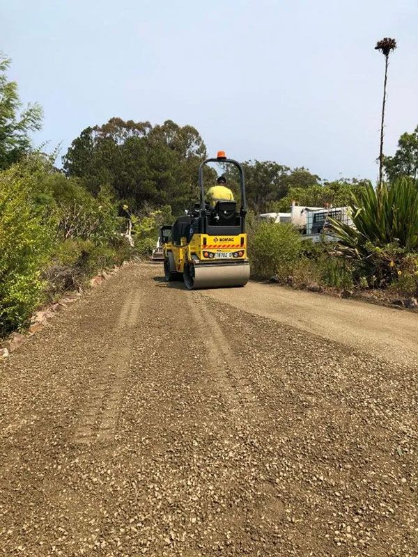 A Yellow Roller is Driving Down a Dirt Road — North Coast Asphalts in Corindi Beach, NSW