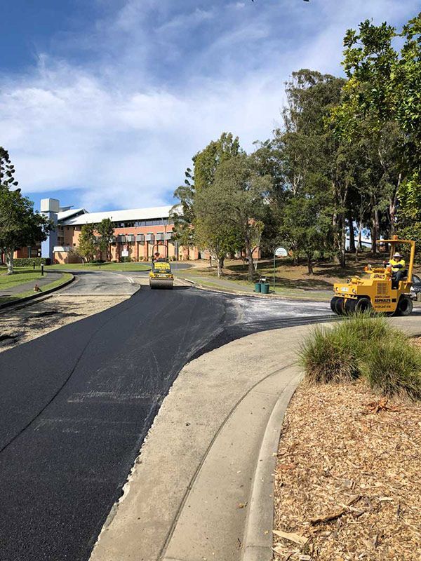 A Yellow Truck is Driving Down a Road Next to a Sidewalk — North Coast Asphalts in Corindi Beach, NSW