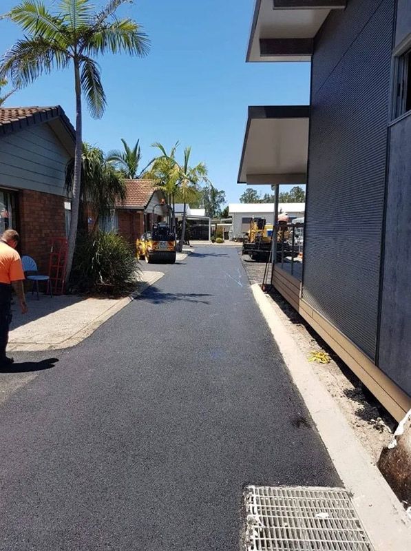 A Man is Standing on the Side of a Road Next to a Building — North Coast Asphalts in Corindi Beach, NSW